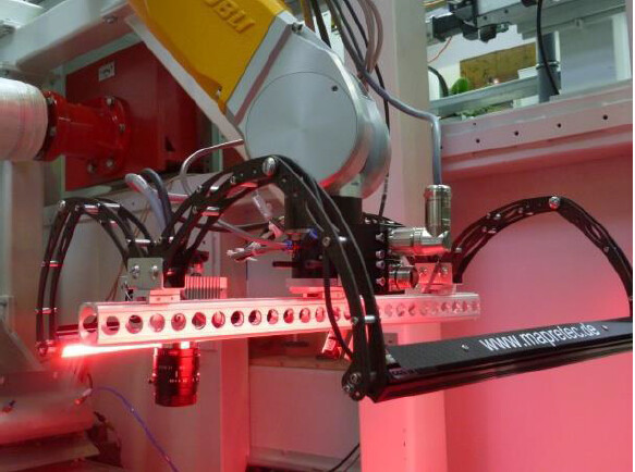Ein gelber Industrieroboterarm mit angebautem Lasermodul in einer Produktionsumgebung.