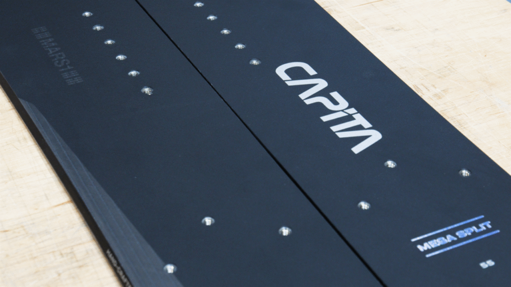 Schwarzes Capita-Splitboard mit sichtbaren Schrauben liegt auf einer hellen Holzoberfläche.
