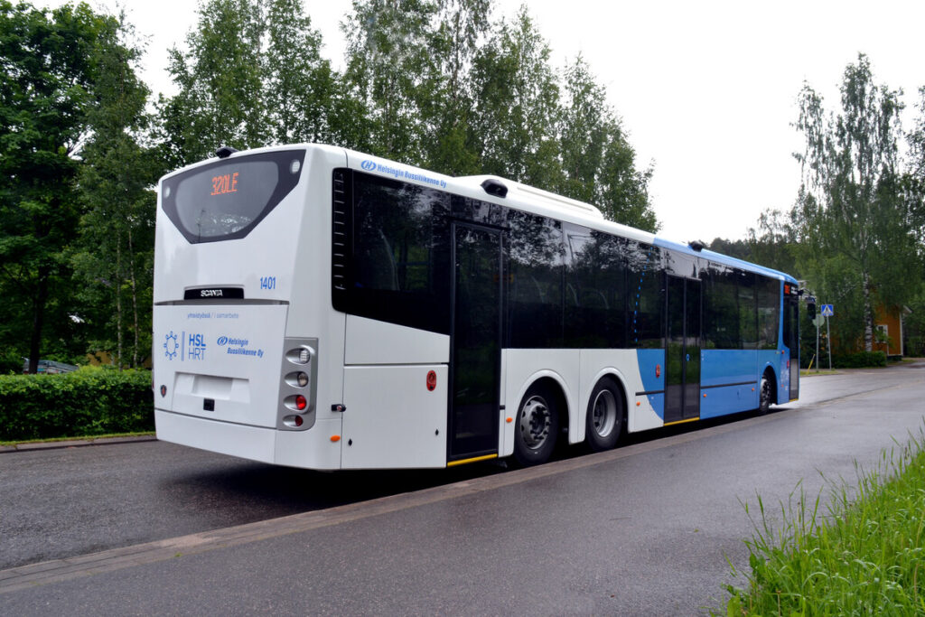 Ein weiß-blauer Stadtbus fährt auf einer von Bäumen gesäumten Straße.