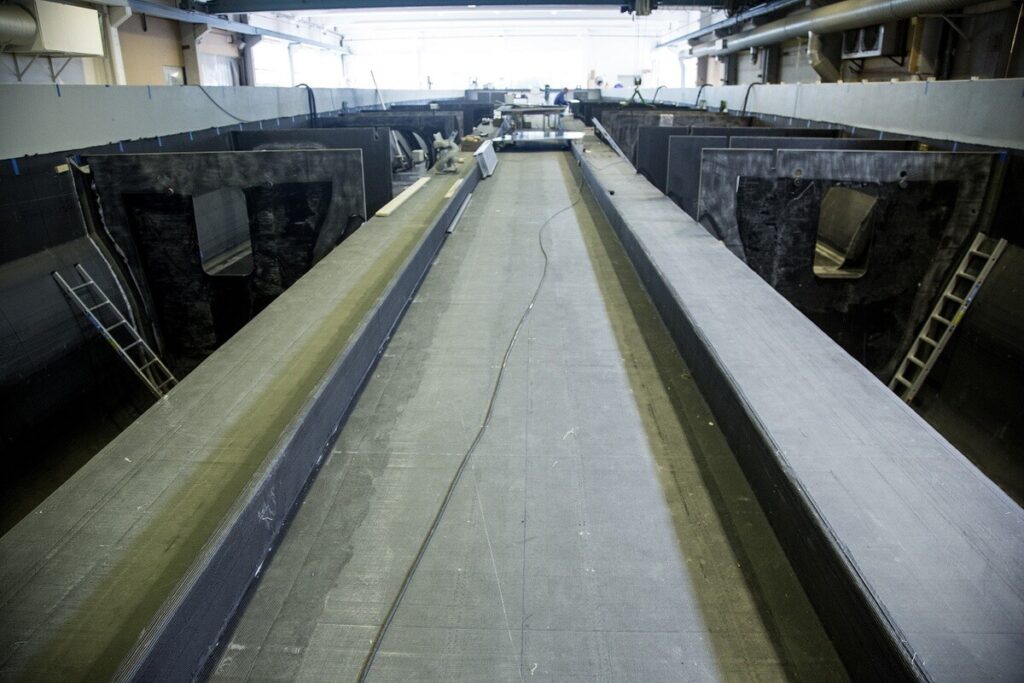 Blick in eine große Industriehalle mit langen, parallel verlaufenden Metall- oder Verbundstrukturen und Leitern an den Seiten.