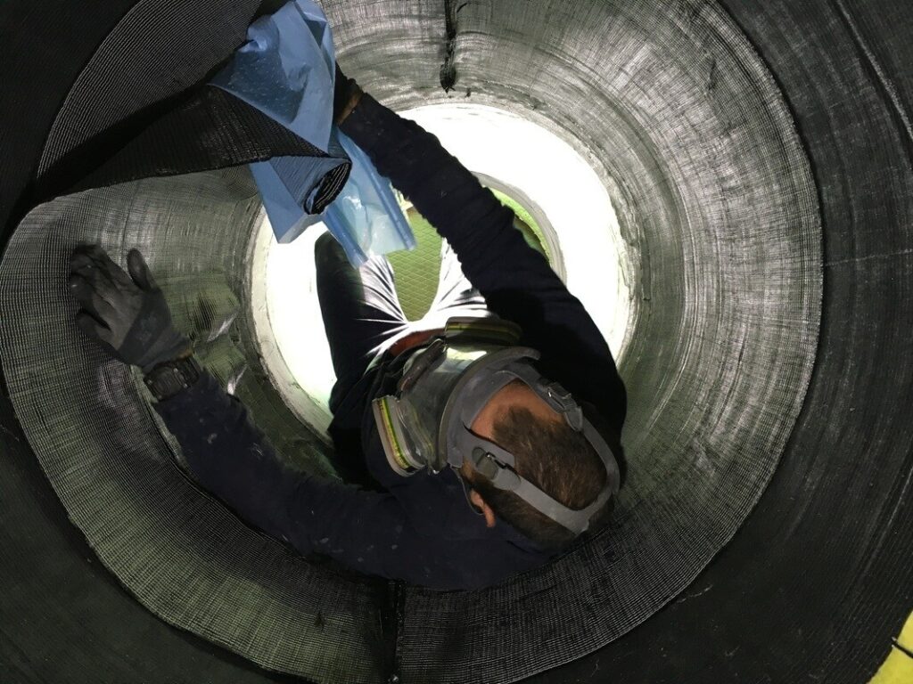 Ein Arbeiter mit Schutzkleidung und Atemschutz arbeitet in einem runden Schacht oder Rohr.