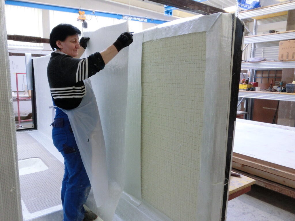 Eine Frau in einer Werkstatt bringt eine Isolier- oder Schutzfolie an einem großen Bauteil an.