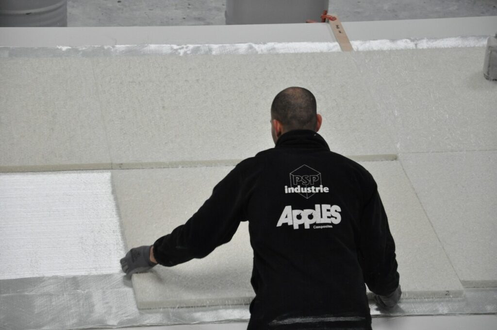 Ein Arbeiter mit schwarzer Jacke verlegt große Dämmplatten auf einer Baustelle.