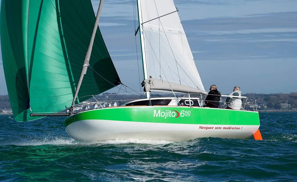 Ein grünes und weißes Segelboot mit gesetzten Segeln auf bewegter See, an Bord zwei Personen.