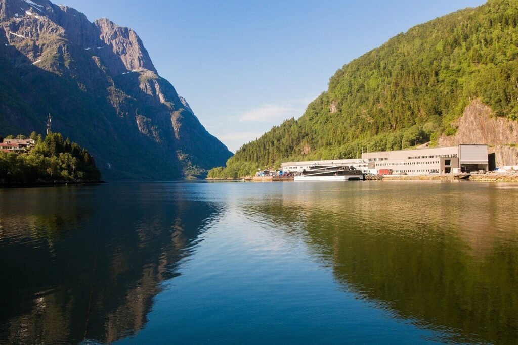 Blick über einen ruhigen Bergsee auf steile Berge und ein Ufer mit Gebäuden