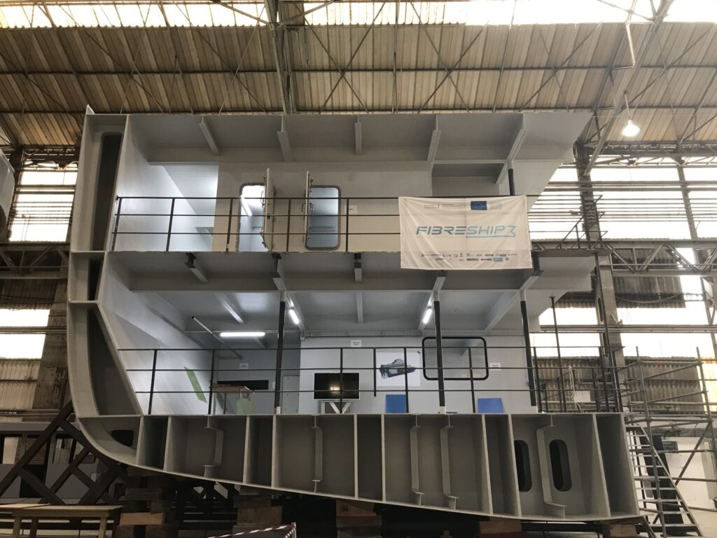 Ein großes Schiffsrumpf-Modell mit mehreren Decks steht in einer Industriehalle.