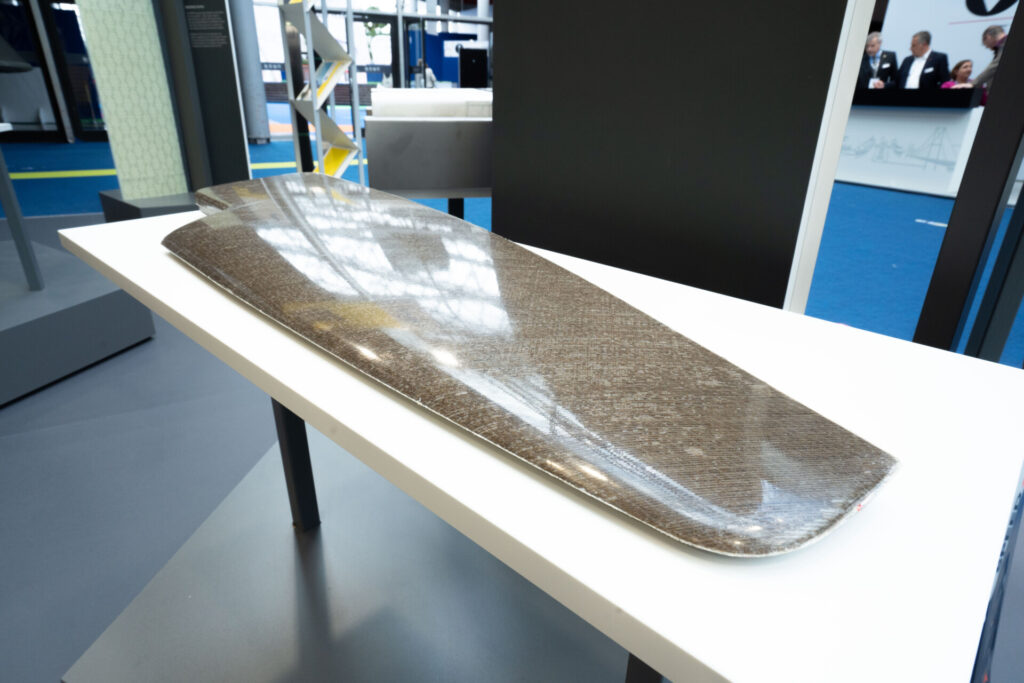 Langes, gebogenes Verbundmaterial-Teil auf einem weißen Tisch in einer Ausstellungshalle.