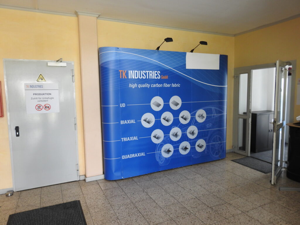 Ein blauer TK-Industries-Messestand steht in einem Gebäude neben einer Tür mit Zutrittsverbot-Hinweis.