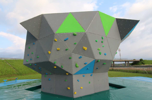 Große graue Kletterwand mit bunten Griffen in geometrischer, katzenähnlicher Form im Freien