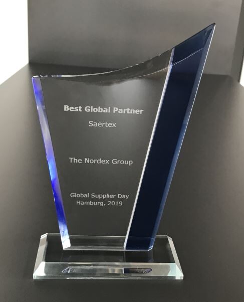 Ein moderner Glaspokal mit der Aufschrift „Best Global Partner“, „Saertex“, „The Nordex Group“ und „Global Supplier Day Hamburg, 2019“.