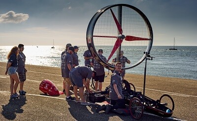 Mehrere Personen stehen neben einem großen, runden Rotorfahrzeug am Strand.