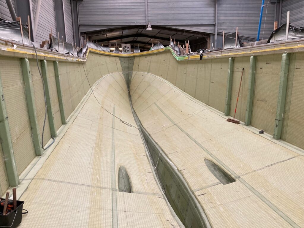Innenansicht eines großen Schiffsrumpfs in Bau mit hellen Bodenplatten und seitlichen Stützen