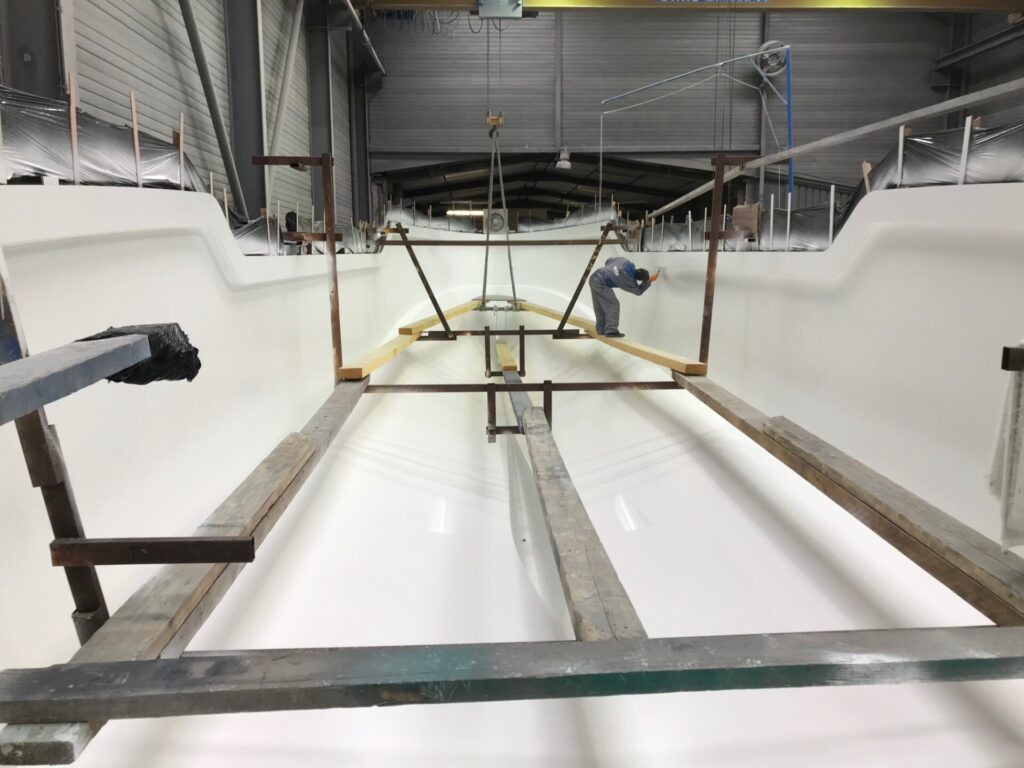 Ein Arbeiter steht in einem großen weißen Industriebehälter und trägt Beschichtung auf, umgeben von Gerüsten und Holzbalken in einer Werkhalle.