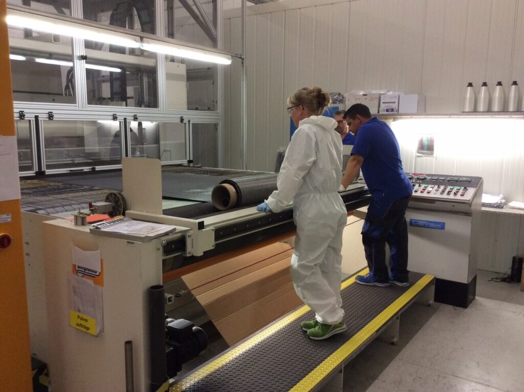 Zwei Personen in Schutzkleidung arbeiten an einer großen Produktionsmaschine in einer Fabrikhalle.