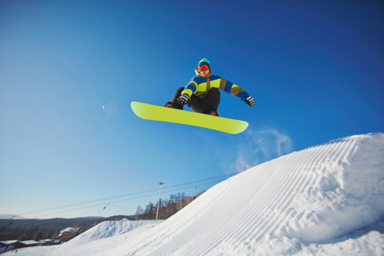 A snowboarder jumps into the air over a mound of snow.