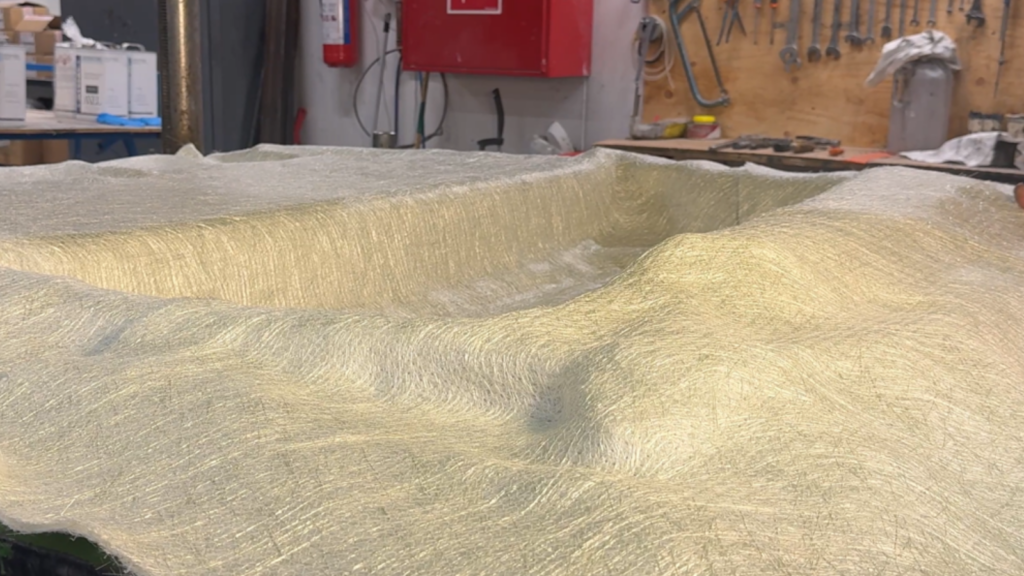 A curved material surface in a workshop with tools in the background.