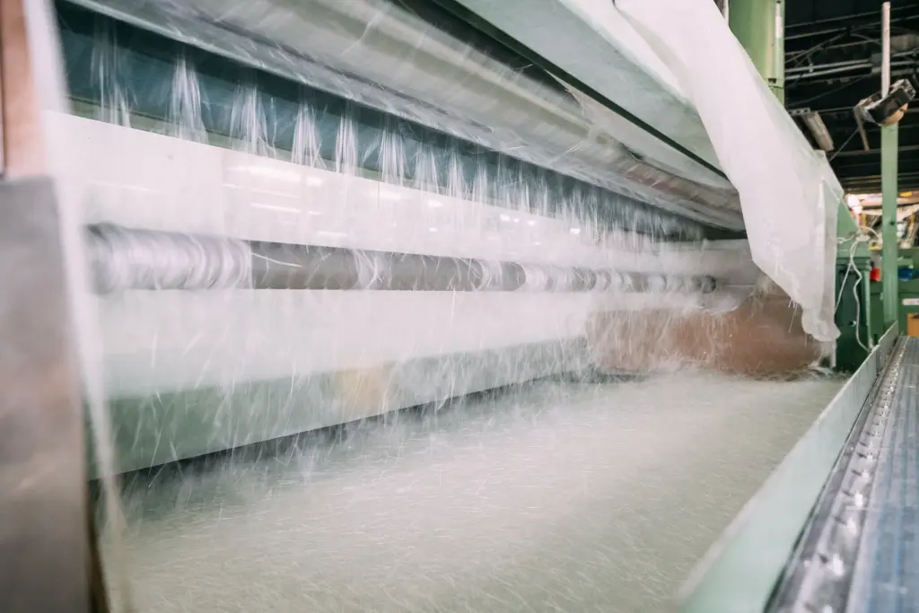 Eine große industrielle Maschine verarbeitet weiße Fasern oder Materialbahnen in einer Fabrikhalle.